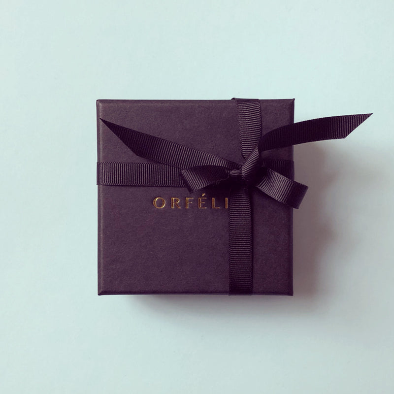 Orfélie jewellery box in matte black with gold logo, placed on a soft green background.