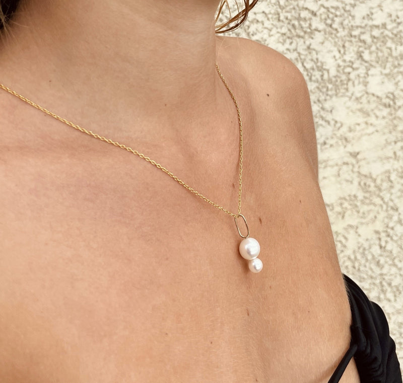 Woman wearing Orfélie Josephine pendant in 18k gold with white freshwater pearls, visible on upper chest with a hint of bikini.